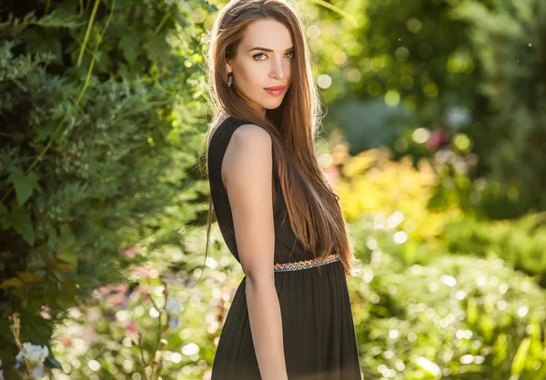 Outdoors portrait of beautiful young woman in luxury black dress posing in summer garden. — Stockfoto