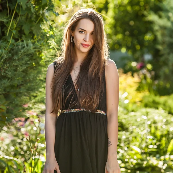 Portrait extérieur de belle jeune femme en robe noire de luxe posant dans le jardin d'été . — Photo