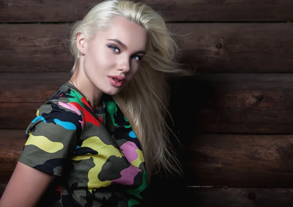 Beautiful young blonde in bright color camouflage undershirt poses on wooden background. — Stockfoto