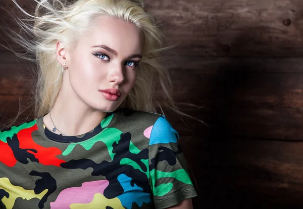 Beautiful young blonde in bright color camouflage undershirt poses on wooden background. — 스톡 사진
