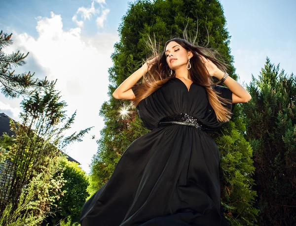 Retrato al aire libre de una hermosa joven en vestido negro largo de lujo posando en el jardín de verano . — Foto de Stock