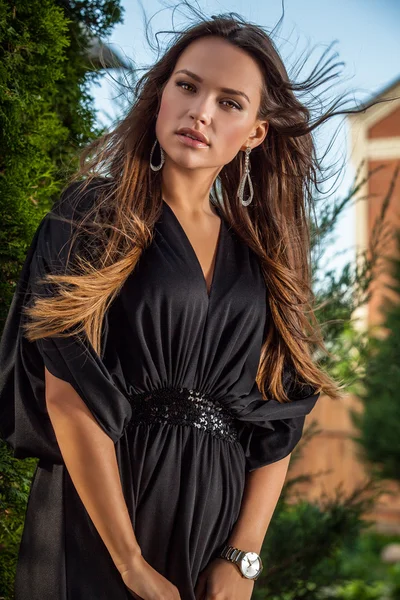 Outdoors portrait of beautiful young girl in luxury long black dress posing in summer garden. — Stockfoto