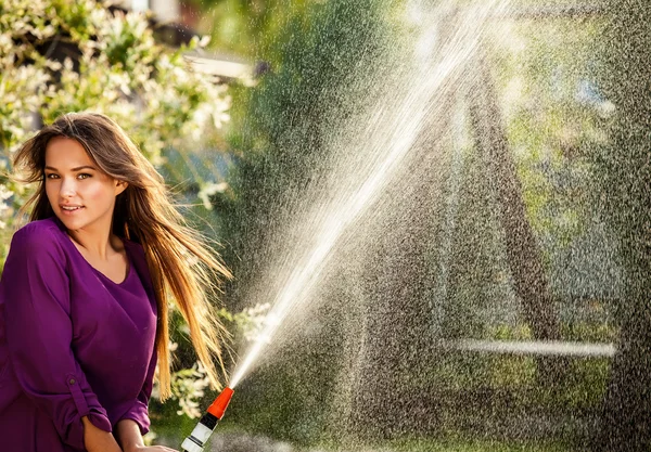 Bella gioiosa ragazza in camicia viola casual posa in un giardino estivo con tubo dell'acqua . — Foto Stock