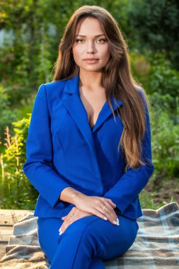 Attractive young woman in official blue suit poses in summer garden.