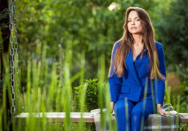 Attractive young woman in official blue suit poses in summer garden. — ストック写真