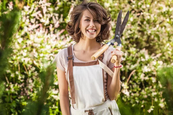 Outdoors portrait of positive young woman in overalls which posing in solar summer garden. — Stockfoto