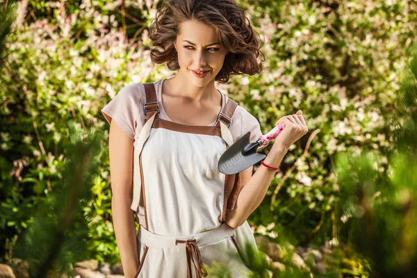 Außenporträt positiver junger Frau in Overalls, die im solaren Sommergarten posiert. — Stockfoto