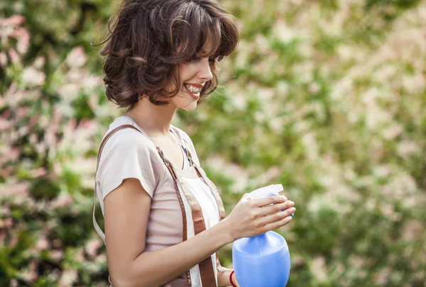 Outdoors portrait of positive young woman in overalls which posing in solar summer garden. — 图库照片