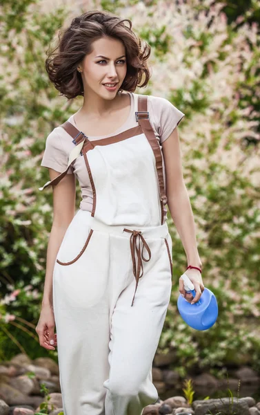 Outdoors portrait of positive young woman in overalls which posing in solar summer garden. — Stok fotoğraf