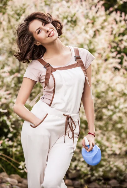 Outdoors portrait of positive young woman in overalls which posing in solar summer garden. — Stok fotoğraf