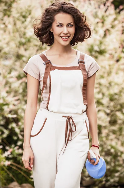 Outdoors portrait of positive young woman in overalls which posing in solar summer garden. — 图库照片