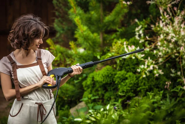 Портрет красивой молодой женщины в комбинезоне, который позирует с водяной пушкой в летнем саду . — стоковое фото