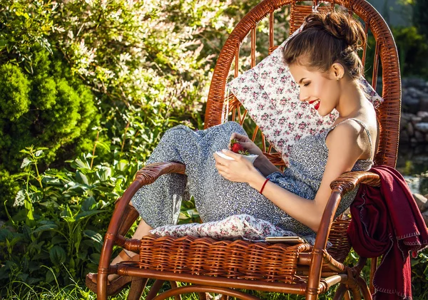 Outdoors portrait of beautiful young woman which sitting in rattan rocking-chair in evening summer garden. — Zdjęcie stockowe