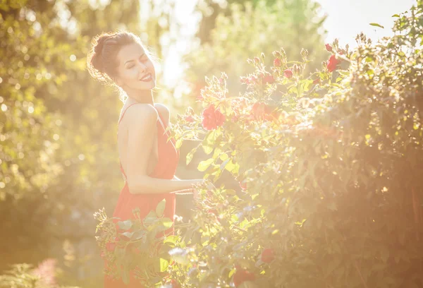 Outdoors portrait of beautiful young brunette girl in luxury red dress posing in summer garden. — Stock Photo, Image