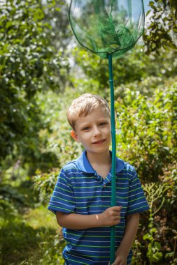 Outdoor portrait of happy little boy with net for butterflies posing in summer garden.