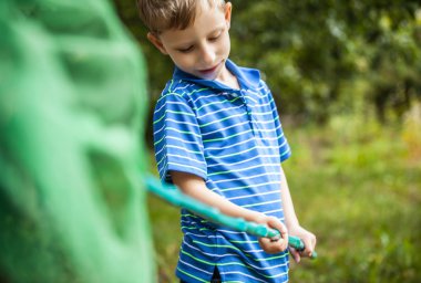 Outdoor portrait of happy little boy with net for butterflies posing in summer garden.
