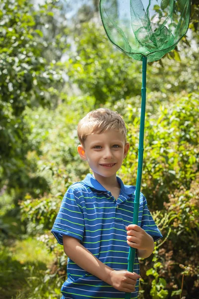 Außenporträt des glücklichen kleinen Jungen mit Netz für Schmetterlinge posiert im Sommergarten. — Stockfoto