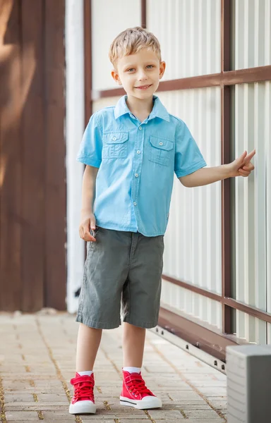 Außenporträt eines glücklichen kleinen Jungen in der Nähe eines mechanischen Metalltors. — Stockfoto