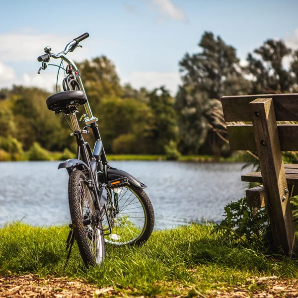Bicicleta perto de banco e lagoa — Fotografia de Stock