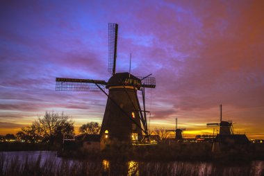 Hollanda, Kinderdijk 'te gün batımında yel değirmenleri ve su kanalları.