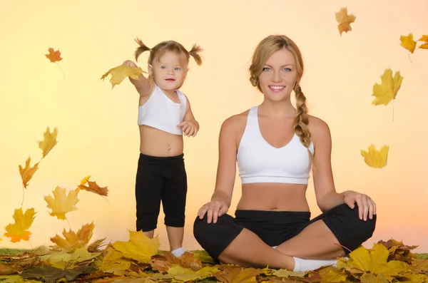 Güzel kadın ve çocuk yoga yaprakları altında yapmak — Stok fotoğraf