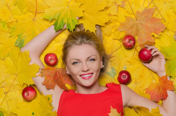 Hermosa mujer en hojas de otoño amarillo y manzanas — Foto de Stock