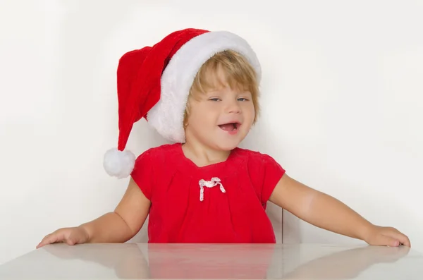 Meisje in kostuum van de Kerstman aan tafel en glimlachen — Stockfoto