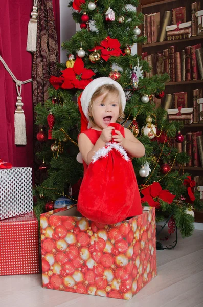 Child dressed as Santa in box with gift bag — Stock Photo, Image