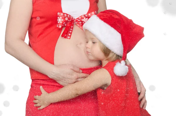 Ребенок обнимает живот беременной женщины на Рождество, снежинки — стоковое фото