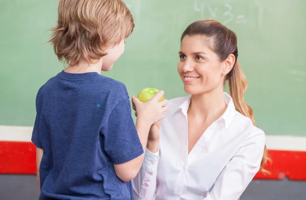Учительница со школьником, подающим яблоко — стоковое фото