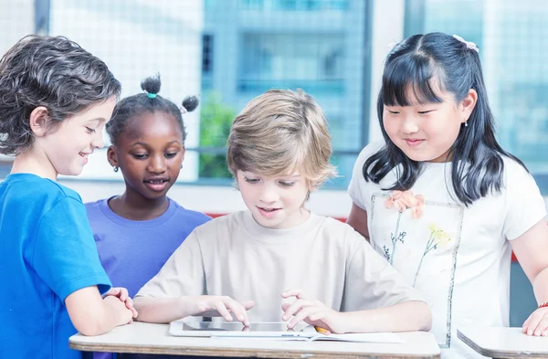 Group of multi ethnic elementary students working with tablet at — Stock Photo, Image