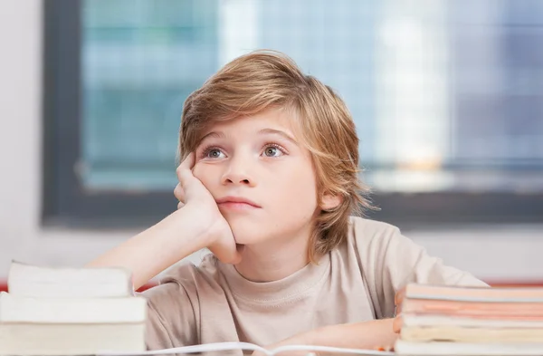 Schoolboy thinking with his books in classroom — Stock Photo, Image