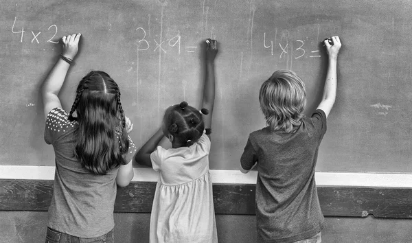 Multi ethnic primary school classroom writing with chalk at blac — Stock Photo, Image