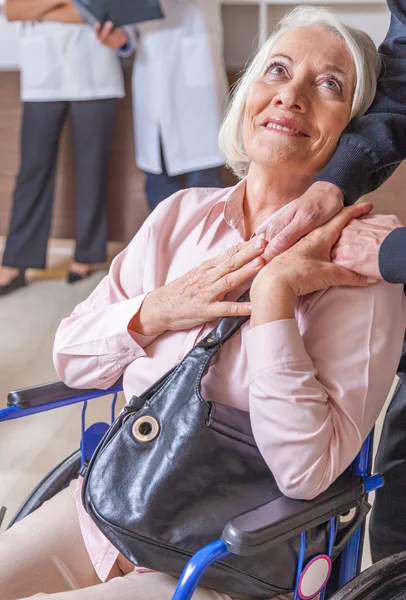 Femme sur 60 ans en fauteuil roulant donnant la main au mari — Photo