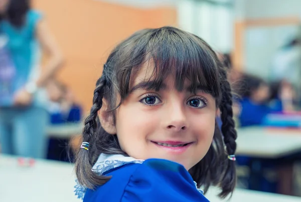 Schoolgirl with forced smile at her classroom desk — Stock Photo, Image