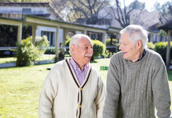 Homens aposentados felizes falando ao ar livre em um jardim de instalações de reabilitação — Fotografia de Stock