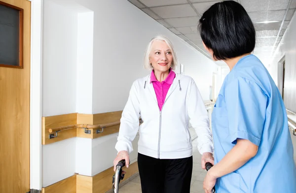 Oudere gepensioneerde vrouw, bijgestaan door nurse in rehab faciliteit — Stockfoto