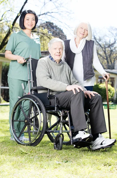 Elder people with wheelchair assisted by nurse outdoor — Stock Photo, Image