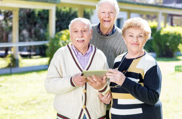 Three elder people using tablet outdoor