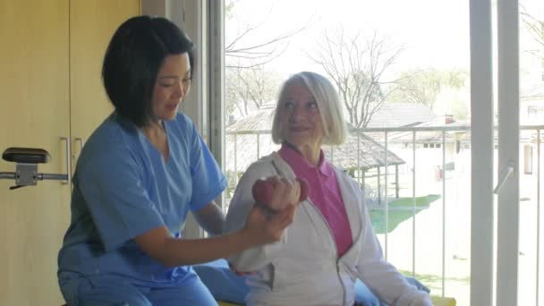 Médica asiática ajudando a mulher idosa no hospital movendo seu braço. Movimento lento — Vídeo de Stock