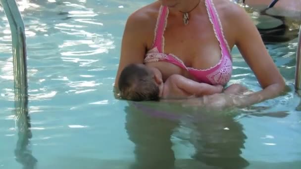 Молодой ребенок сосет молоко из материнской груди в бассейне — стоковое видео