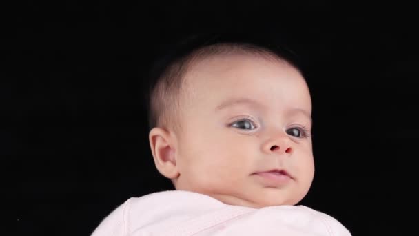 Jonge baby bewegen en het maken van grappige gezicht uitdrukkingen tegen een zwarte achtergrond — Stockvideo