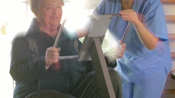 年轻的非洲护士帮助老年妇女在康复健身房与腿机器。从后面发出的光芒 — 图库视频影像