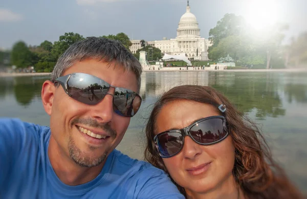 Happy tourist couple smiling for a selfie in front of Washington Capitol, USA