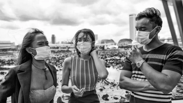Three asian young friends standing outdoor in the city talking and wearing face masks in covid coronavirus pandemic.