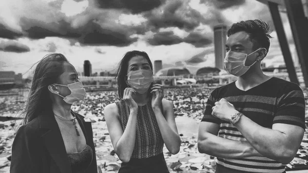 Three asian young friends standing outdoor in the city talking and wearing face masks in covid coronavirus pandemic.