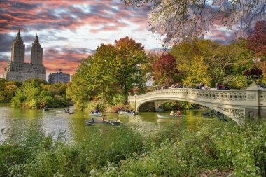 Bow Köprüsü ve Central Park 'taki Göl' ün üzerinde inanılmaz bir gün batımı. New York şehrinin yeşillik renkleri.