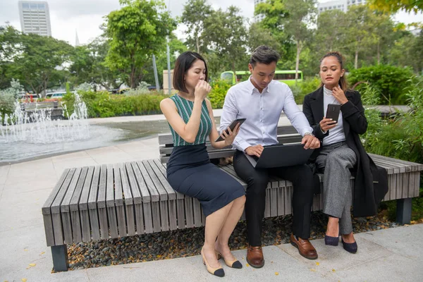 屋外ビジネスミーティング 1人のアジア人男性と2人のアジア人女性が公共のベンチに座ってビジネスの詳細を議論する — ストック写真