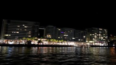 Gece dairesel rıhtım binaları, hareket halindeki bir teknenin manzarası, Sydney. Yavaş çekim
