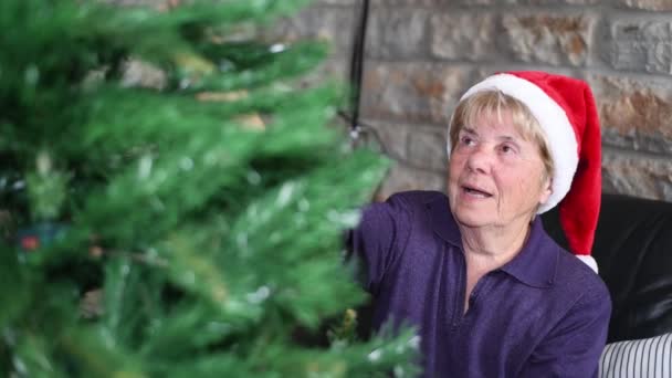Idős nyugdíjas nő díszítő karácsonyfa otthon visel Mikulás kalap — Stock videók